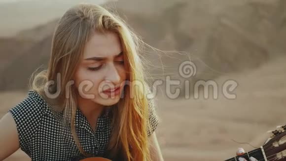 在沙漠风景沙漠山脉背景慢动作中弹吉他和唱歌的女性视频的预览图