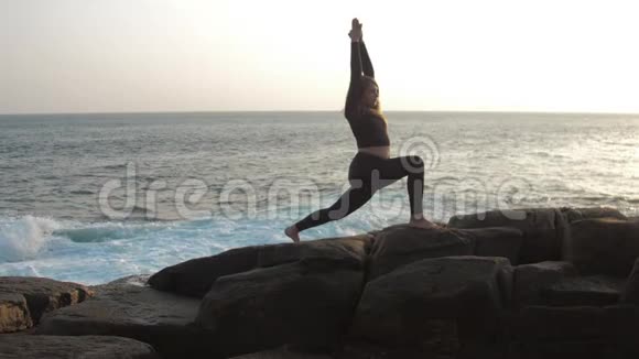 女孩剪影练习瑜伽锻炼站在岩石上视频的预览图