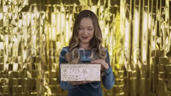 快乐兴奋的女孩打开一个盒子带着礼物金色的光从盒子里照在她的脸上一个金色背景的女人4千克视频的预览图