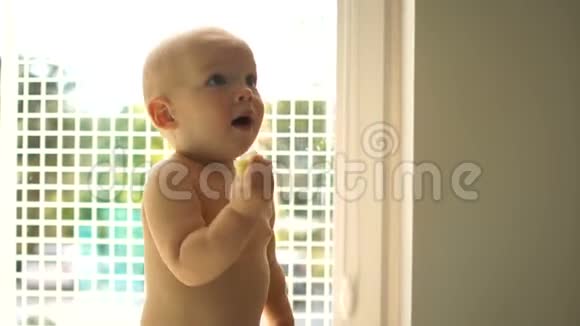 可爱的一岁半快乐宝宝独自在家窗前坐在地板上吃一个苹果视频的预览图