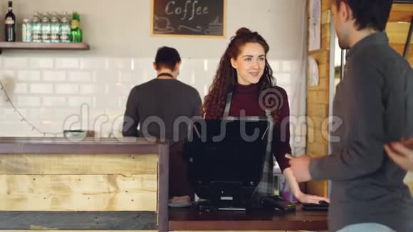 年轻顾客在咖啡屋点外卖咖啡用智能手机付款而女收银员则接受视频的预览图