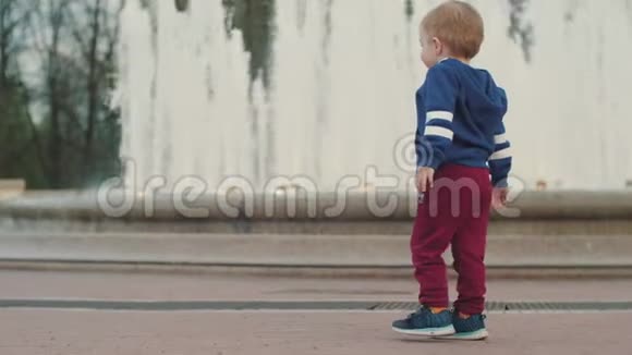 一个小男孩在喷泉前散步与父母同行父母照顾公园周末视频的预览图