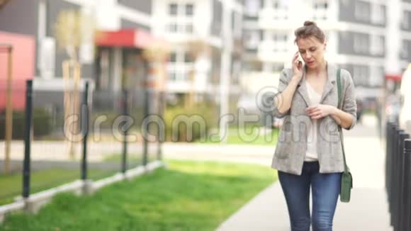 漂亮的年轻女人带着智能手机和她的儿子在一条城市街道上散步好奇的学生骑着电动滑板车视频的预览图