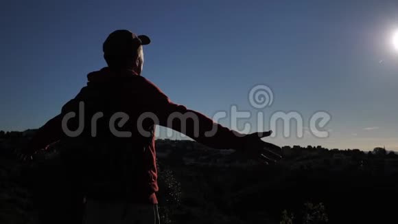 一个男人的剪影站在上面看着这座城市在日落时举起双手对着太阳视频的预览图