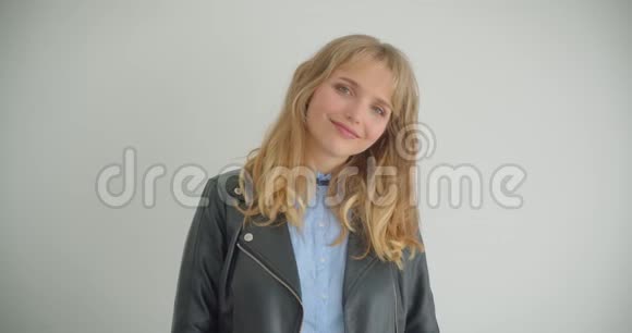 漂亮的金发女孩穿着皮夹克对着镜头摆出害羞的微笑孤立在白色背景上视频的预览图