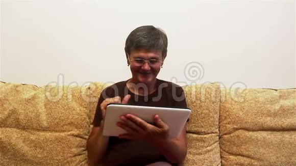 一位有魅力的成年女性正在与家人视频聊天在平板电脑上坐在家里的沙发上视频的预览图