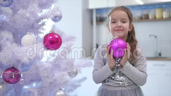 漂亮的小女孩正向相机伸出粉红色的宝布尔站在圣诞树附近微笑着视频的预览图
