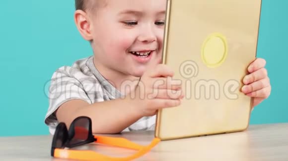 特写脸可爱的小孩子用平板电脑坐在桌子上隔离在蓝色上视频的预览图