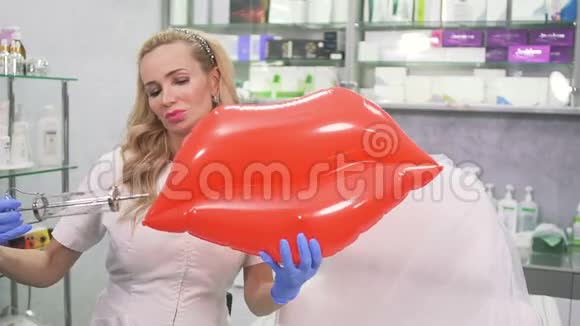 美容诊所里带玩具嘴唇和注射器的迷人医生为相机摆姿势视频的预览图