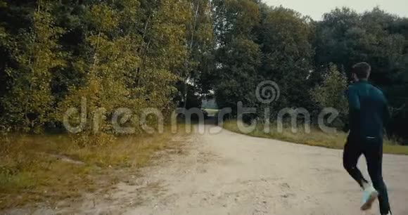 运动员跑到一个森林道路开口无人机后视图坚定的运动员在秋天穿越乡间小路视频的预览图