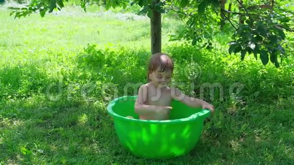 微笑的婴儿洗澡在户外的小浴缸里飞溅视频的预览图