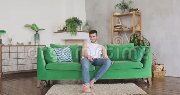 年轻夫妇在客厅的绿色沙发上男人想看电视女人拥抱他视频的预览图