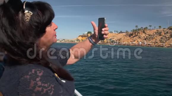 在热带岛屿附近的一艘船上老年女性成人游客使用智能手机进行视频通信这就是视频的预览图
