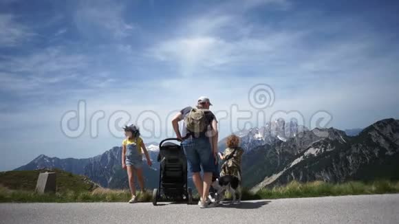 父母和三个孩子一家人带着一个小孩在婴儿车里从侧面欣赏美丽的山景视频的预览图