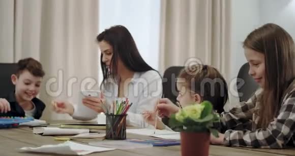 成熟和现代的母亲帮助她的孩子做家庭作业用平板电脑解决问题他们坐在一个大房间里视频的预览图