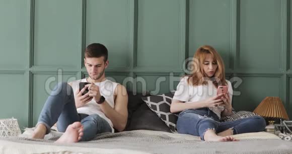 年轻夫妇正在家里的床上浏览智能手机视频的预览图