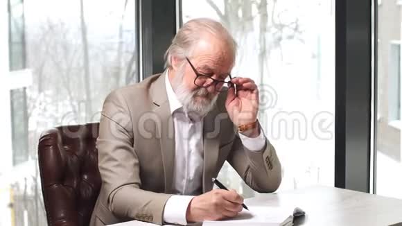 老教授头发灰白胡子留着漂亮的西装在笔记本上记笔记视频的预览图