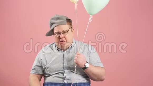 穿着灰色休闲服的哭泣的成年男子的肖像在粉红色的衣服上拿着气球视频的预览图