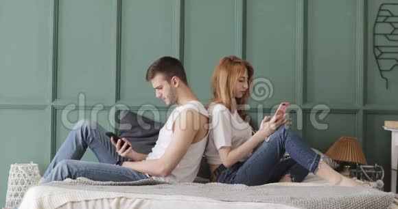 男人和女人坐在床上互相背着浏览他们的手机视频的预览图