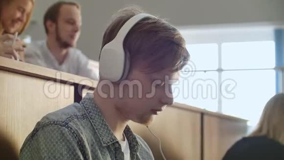 在大学礼堂里一个男生在休息时不注意就用白色耳机听音乐视频的预览图