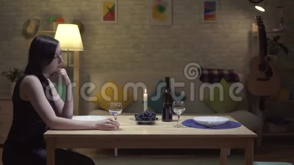 孤独可爱的黑发女人坐在一张桌子旁在现代的房子里烛光下哭泣视频的预览图