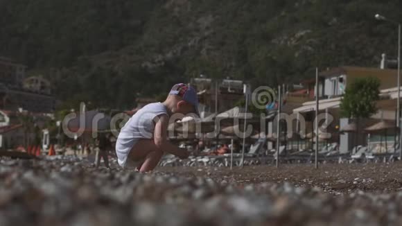 一个小男孩站在海边向水中扔一颗鹅卵石慢动作视频的预览图