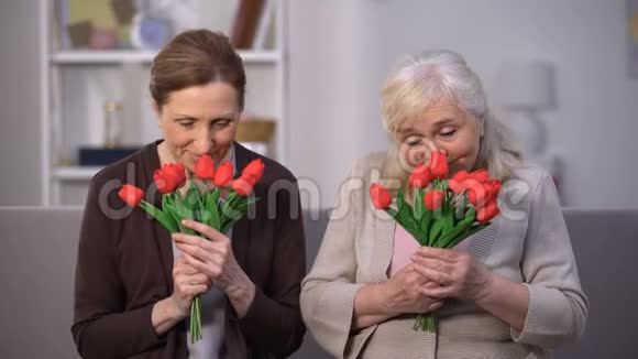 微笑的老年妇女嗅着郁金香花束快乐的母亲节礼物视频的预览图