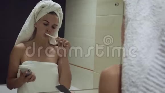 年轻的女人刷牙看着智能手机视频的预览图