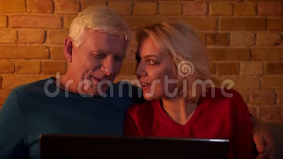 在舒适的公寓里坐在沙发上一对爱老的幸福夫妇用笔记本电脑带着喜悦的笑容特写镜头视频的预览图