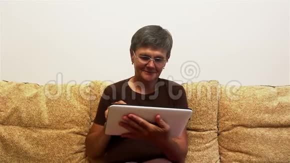 一位有魅力的成年女性正在与家人视频聊天在平板电脑上坐在家里的沙发上视频的预览图