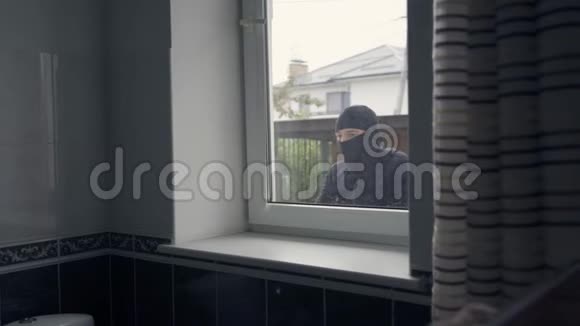 穿着黑色衣服和巴拉克拉瓦的小偷从窗户闯进了房子犯罪概念视频的预览图
