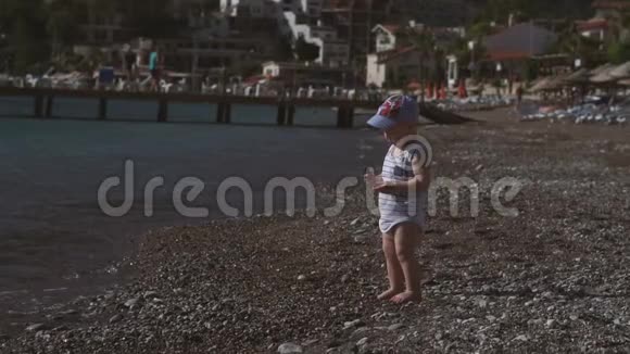 一个可爱的蹒跚学步的孩子站在海边把一颗鹅卵石扔进水里慢动作视频的预览图