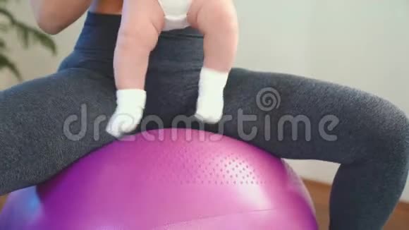 快乐的妈妈在玩婴儿在大球上做婴儿健身运动视频的预览图