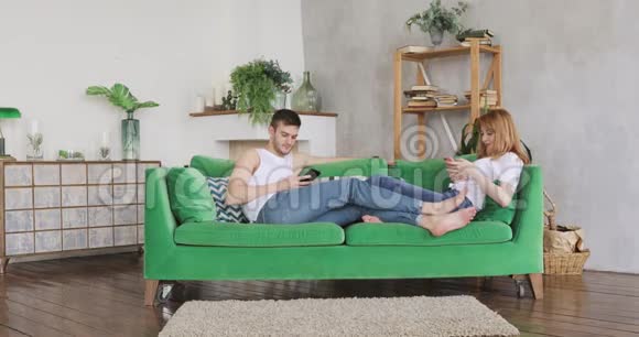 年轻夫妇正坐在绿色沙发上浏览智能手机视频的预览图