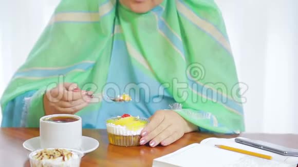 一个身穿浅绿色围巾的年轻穆斯林妇女在咖啡馆里吃蛋糕和喝茶视频的预览图