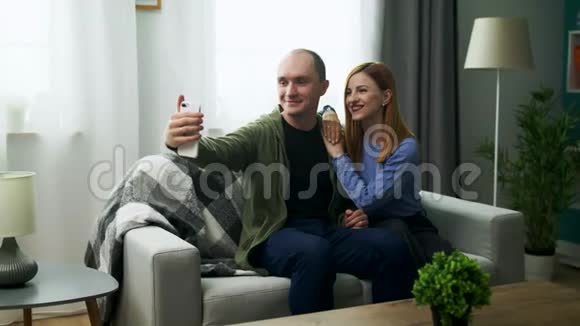 年轻人和女友在客厅里用手机摄像头自拍视频的预览图