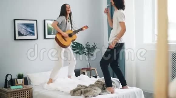 快乐的学生在家里用遥控器唱歌弹吉他在床上跳舞视频的预览图