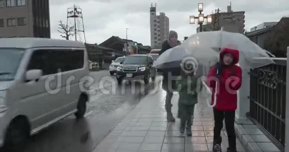 小女孩带着一把透明的塑料伞在一个寒冷潮湿下雨的日子里和家人一起穿过日本的一座桥视频的预览图