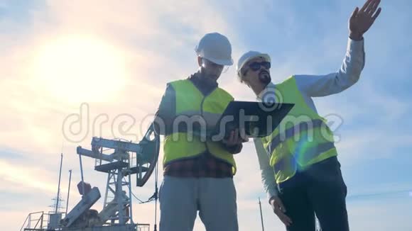 两名男性专家在石油钻井平台附近的一个石油生产现场的工作过程油泵视频的预览图