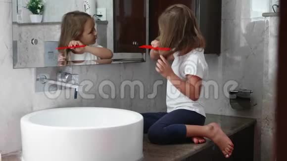 小金发女孩在浴室的镜子前梳头视频的预览图