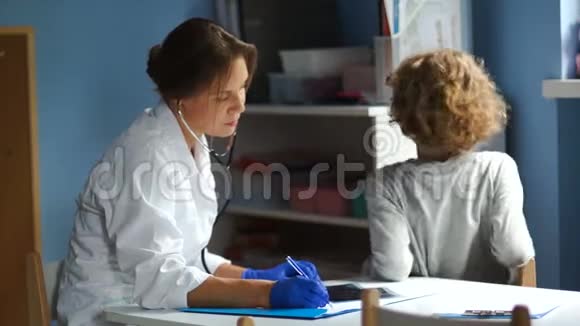 儿科医生在接待处为学生检查用听诊器从后面听肺部视频的预览图
