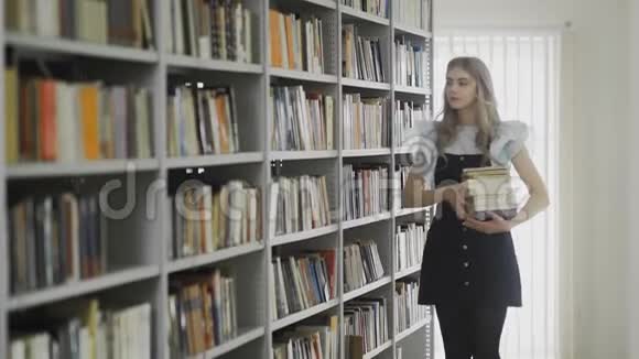 年轻漂亮的金发女学生手里拿着许多书走进大学图书馆视频的预览图
