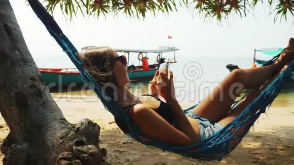 女人正躺在沙滩上的智能手机吊床上浏览网页视频的预览图