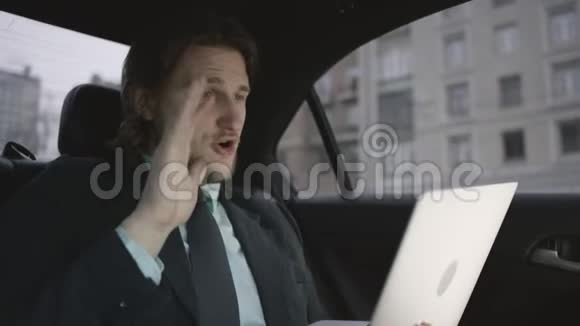 一个英俊的男人棕色头发穿着开心果衬衫灰色西装坐在车里在笔记本上工作视频的预览图