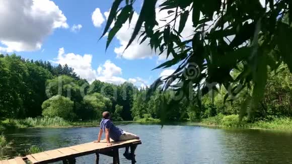 为生活放松自然疗法理念年轻人坐着放松一边在水面附近摆脚视频的预览图