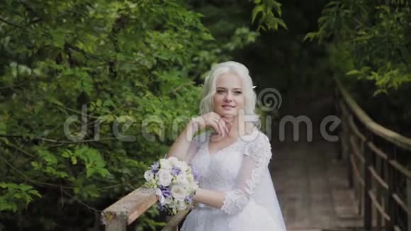 美丽的金发新娘在靠近森林栏杆的桥上视频的预览图