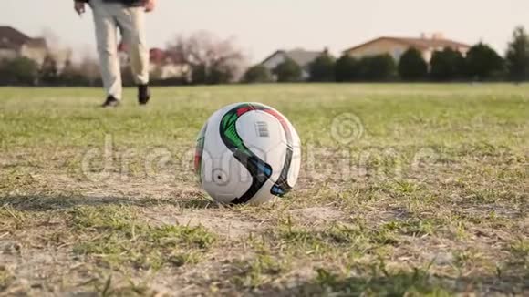 年轻的父亲在和儿子踢足球时踢足球然后沿着运动场的慢动作跑视频的预览图
