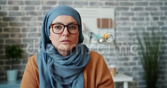 戴着头巾眼镜的独立穆斯林女孩在办公室里看镜头的画像视频的预览图