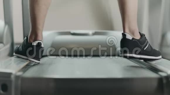 在健身健身房的跑步机上近距离的脚开始跑步黑鞋的背面视频的预览图