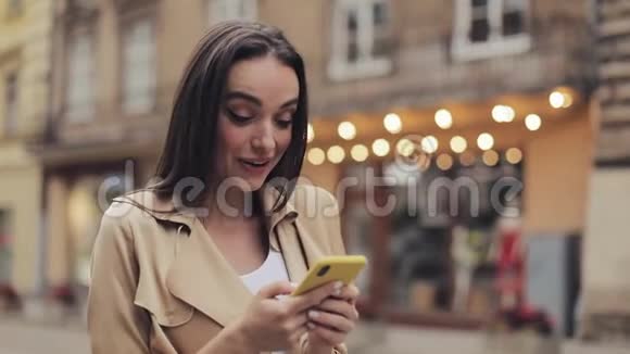年轻迷人的女孩拿着手机聊天和笑说哇站在城市背景关闭视频的预览图